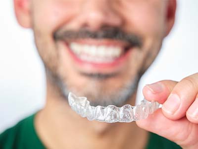 A man holding up a clear plastic tray with a set of transparent braces.