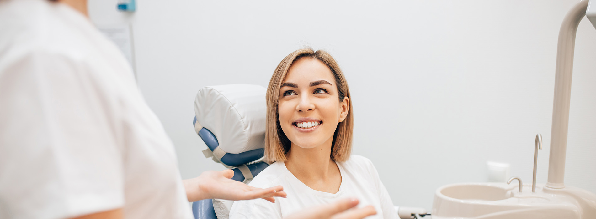 The image shows a woman sitting in a dental chair with a smile on her face, receiving dental care from a dentist who appears to be adjusting her mouthpiece.