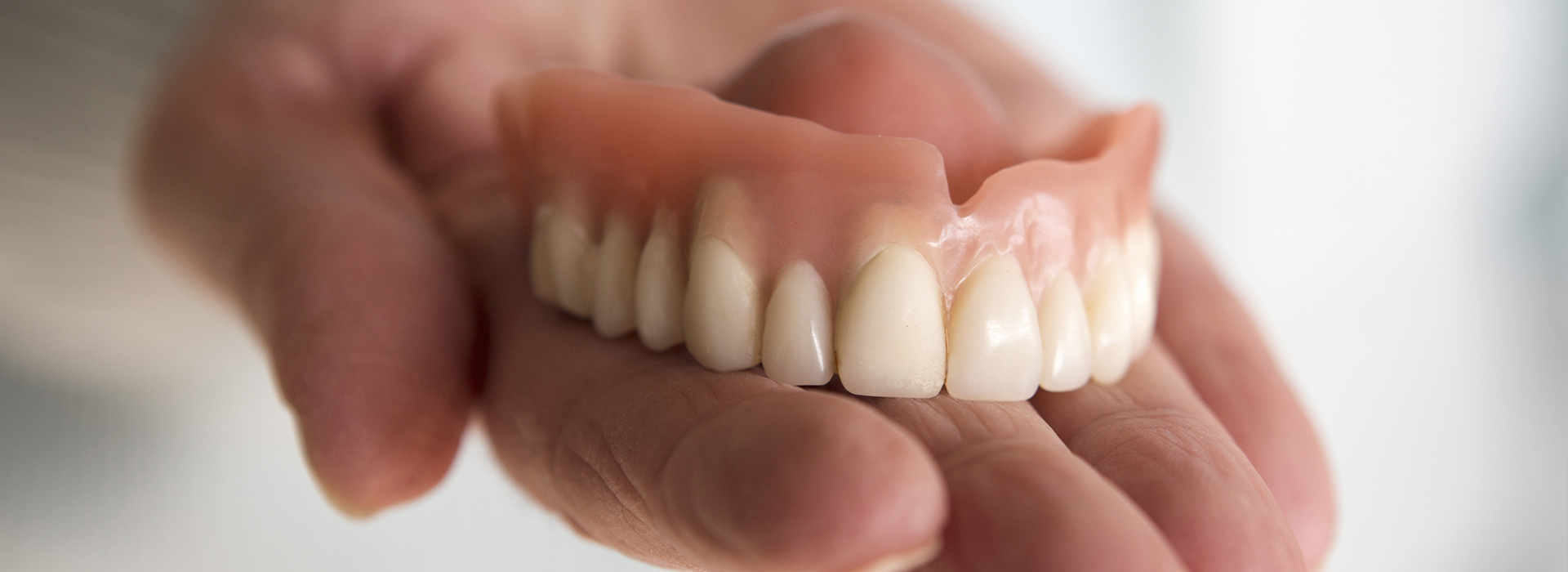 A person s hand holding an upper denture with multiple teeth.