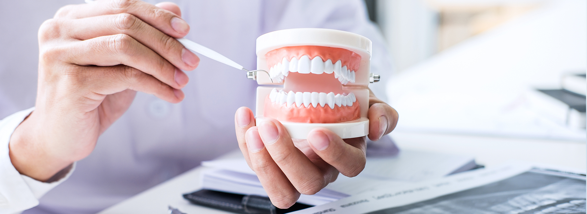 A person holding a toothbrush with toothpaste over a cup of water while another person looks on, both in a professional setting.