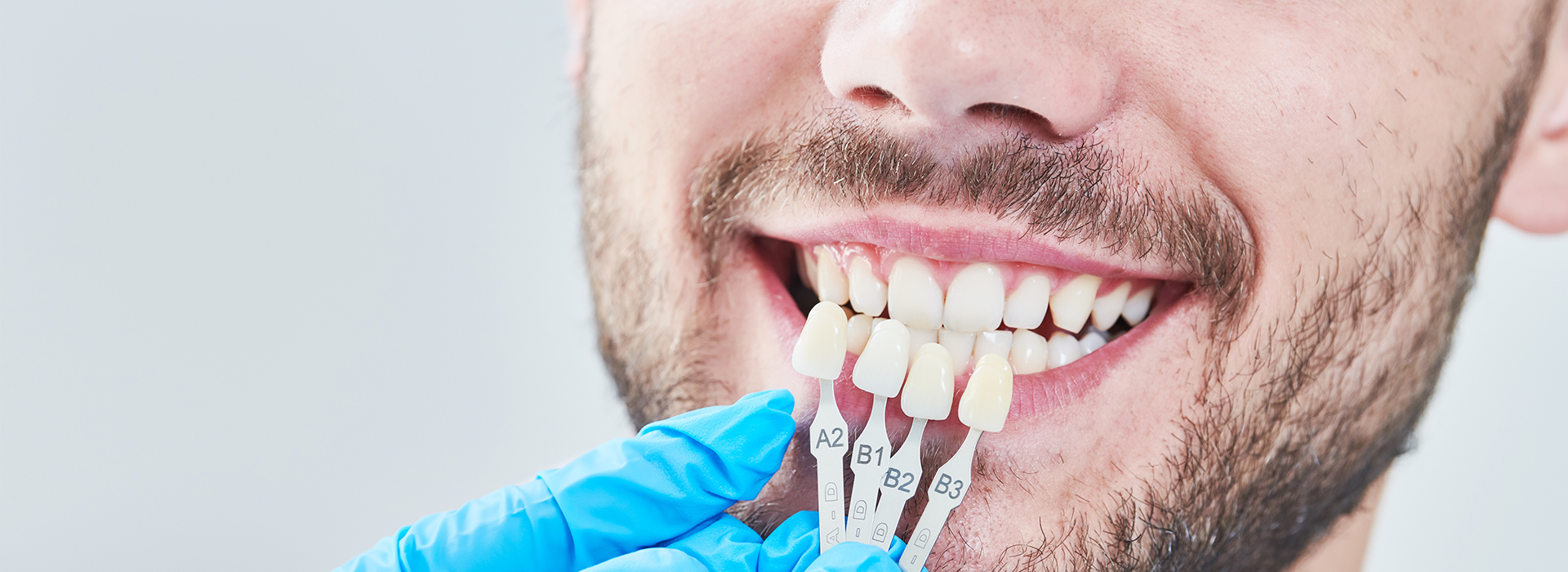 A man with a toothy smile holding a toothbrush near his mouth, set against a blurred background with medical equipment.