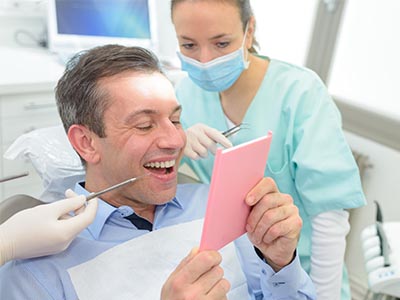 A dentist holds up a tablet with a surprised expression while surrounded by dental equipment and a smiling dental assistant.