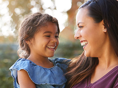 A smiling woman holding a child outdoors during daylight.