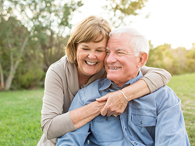 Two elderly people embracing each other outdoors during daylight.