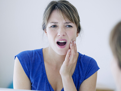 A woman with her hand on her chin, looking into a mirror with an expression of concern or worry.