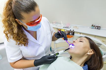 A dental hygienist is performing oral care on a patient using a dental drill.