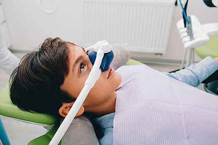 A young person wearing a dental mask with a device attached to their face, sitting in a dental chair.